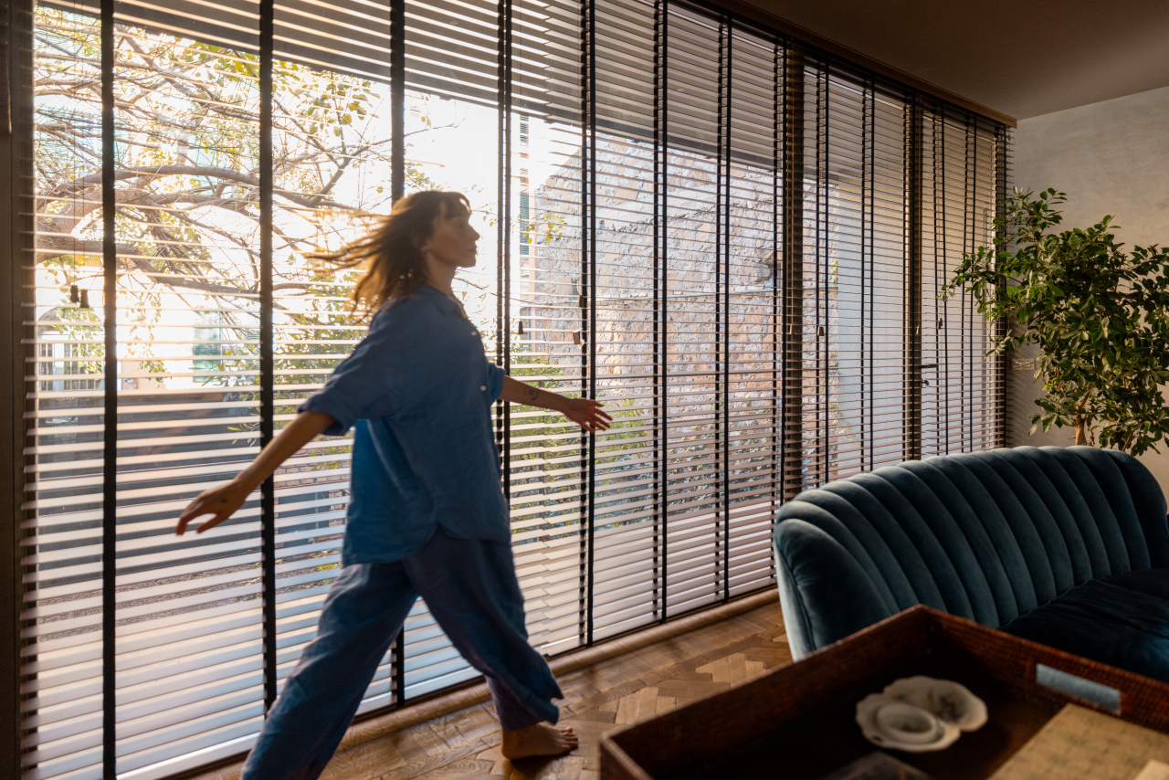 A woman walking past floor-to-ceiling custom blinds in golden light
